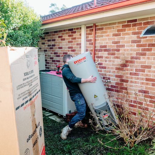 a plumber carrying a hot water tank outside a house in Australia