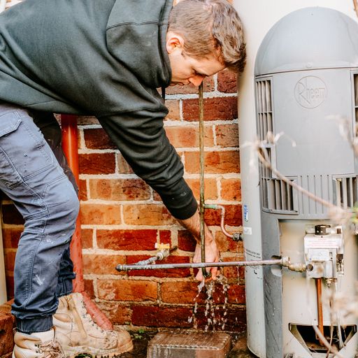 a plumber connecting a hot water tank to water supply outside a house in Australia