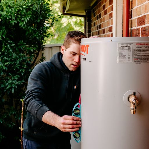 a plumber installing a hot water tank outside a house in australia